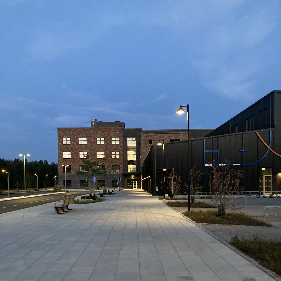 Bild på Hagavikskolan, en ny skolbyggnad med tegelfasad och mörk träpanel. Fasaden har mönstermurningar och ett integrerat konstverk. Entrén är tydligt markerad och skolbyggnaden omges av en grön skolgård.