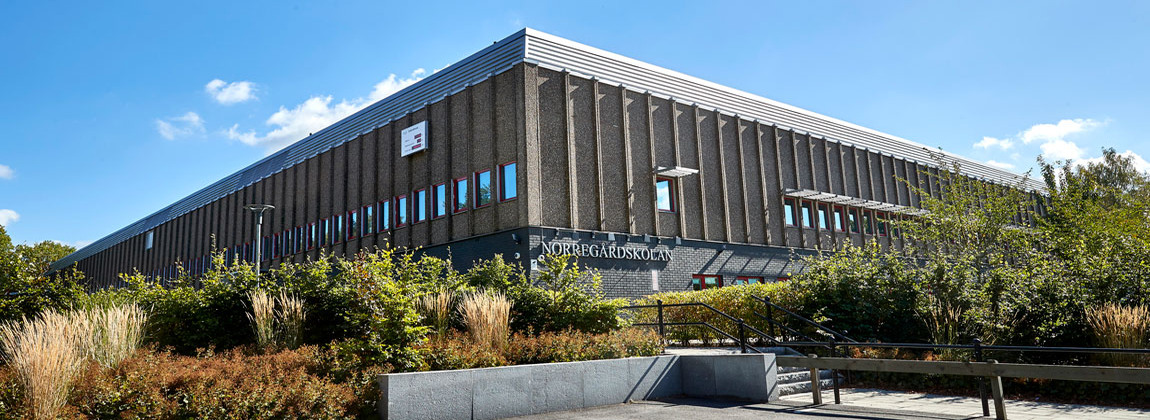 En grå byggnad i sten, på fasaden hänger en skylt där det står Norregårdsskolan på i vita bokstäver