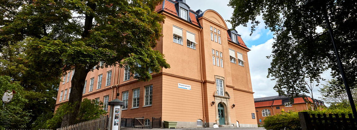 En gammal orange byggnad med flera våningar. Framför byggnaden står två höga träd