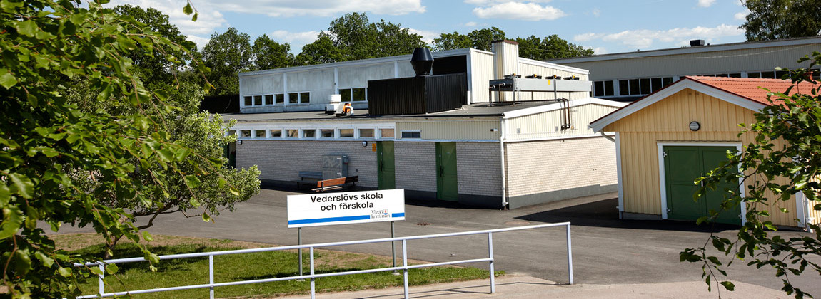 Vit tegelbyggnad med gröna dörrar. Framför byggnaden står en skylt med texten Vederslövs skola och förskola