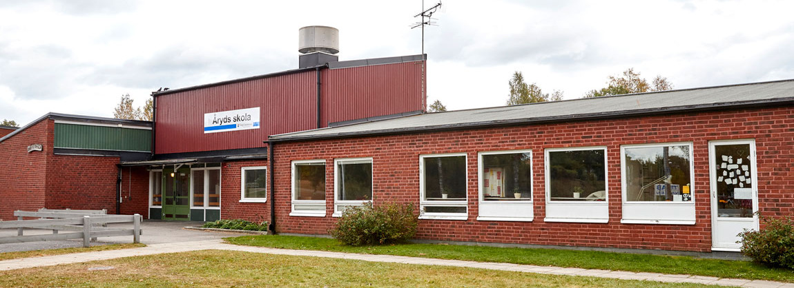 Röd byggnad med grön dörr. På fasaden hänger en skylt med texten Åryds skola