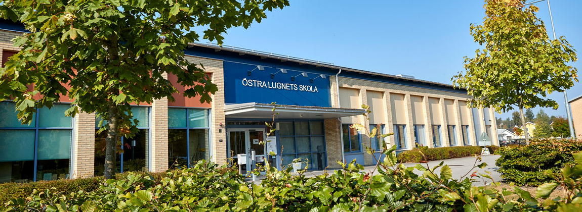 En gul tegelbyggnad. Ovanför dörren hänger en blå skylt med texten Östra Lugnets skola i vita bokstäver