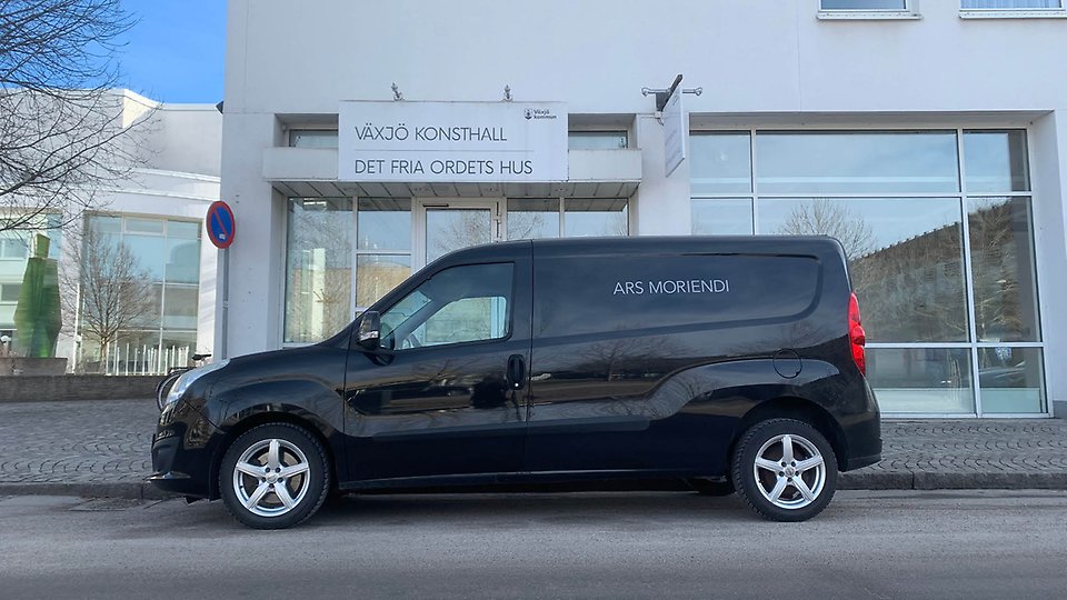 Foto på en svart skåpbil som står utanför Växjö konsthalls entré med loggtexten "Aris Moriendi"